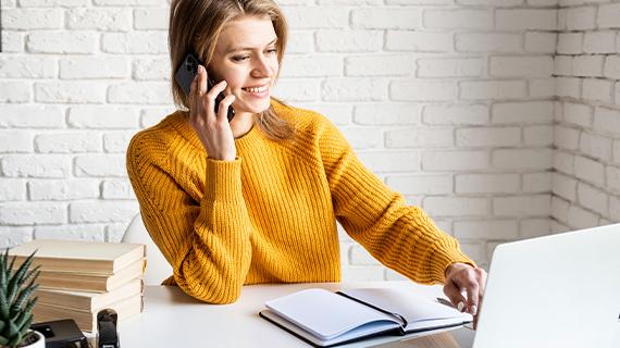 Eine Frau telefoniert am Handy während sie am Schreibtisch am Computer sitzt