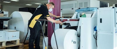 Deutsche-Post-Mitarbeiter steht an großer Druckmaschine und ist konzentriert