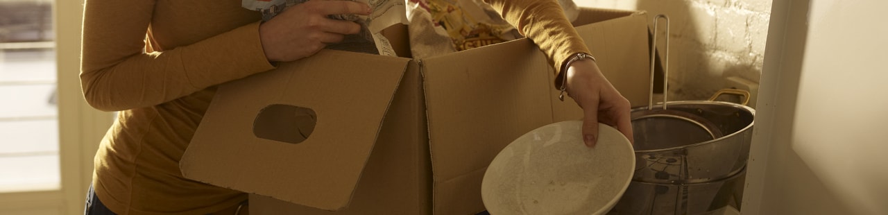 Eine Frau packt einen Umzugskarton mit Geschirr aus.