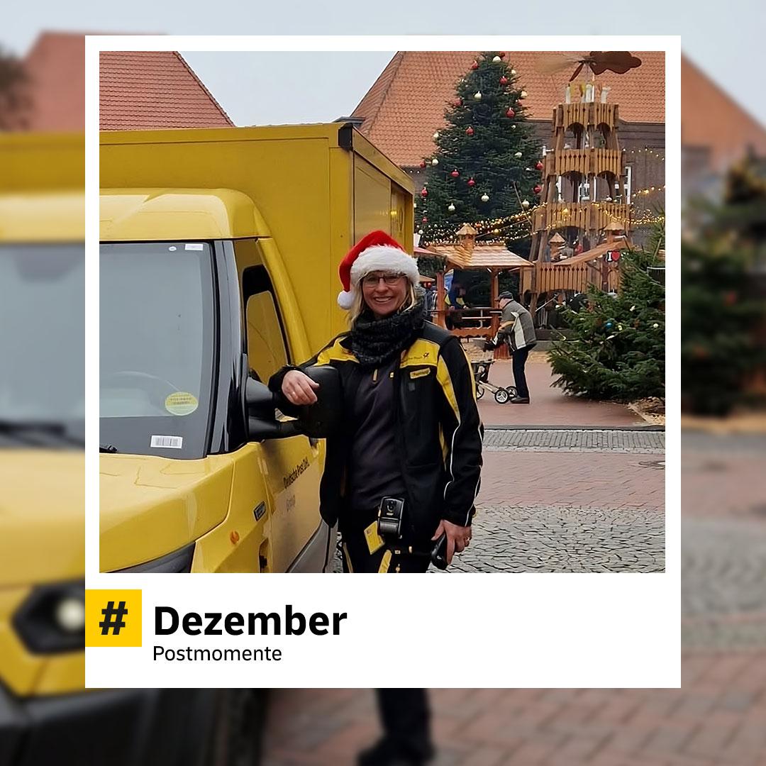 Postzusteller mit Nikolausmütze steht lächelnd neben einem DHL-Zustellfahrzeug. Im Hintergrund weihnachtlich geschmückter Platz mit Tannenbaum und Pyramide. Hashtag: „#Dezember – Postmomente“.