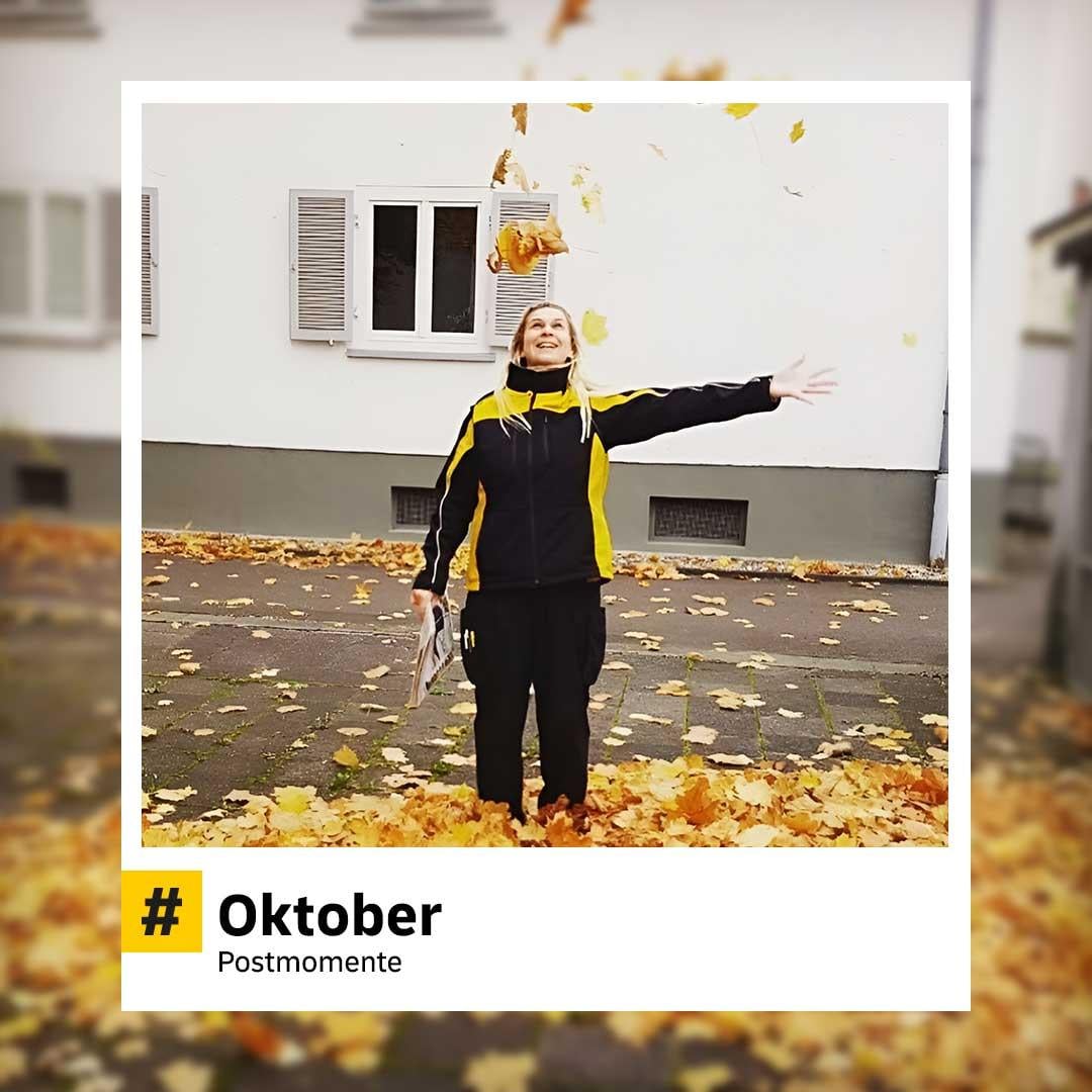Postzustellerin steht lachend auf einem von Herbstlaub bedeckten Gehweg und wirft Blätter in die Luft. Im Hintergrund ein weißes Wohnhaus. Hashtag im Bild: „#Oktober – Postmomente“.